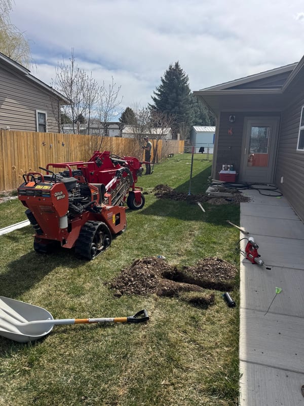 Trencher and an open trench in a side yard next to a house