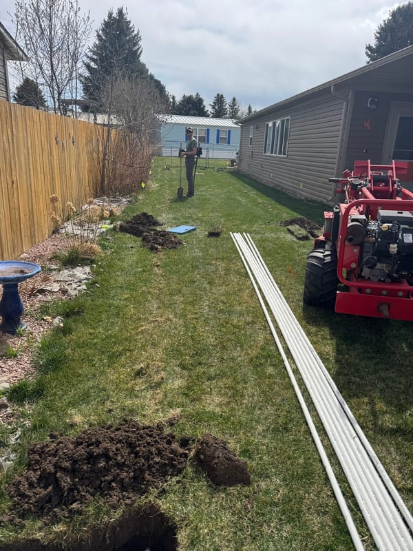 PVC pipe laid along a side yard with a trencher, ready for a sprinkler install