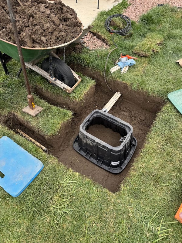 Black sprinkler valve box set in an excavated hole in a lawn