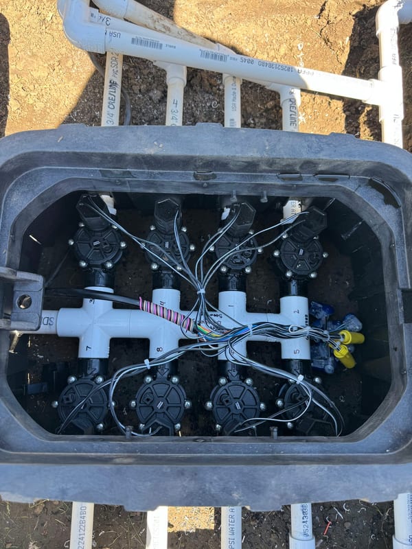 Six sprinkler valves on a manifold inside a valve box, wired for the controller