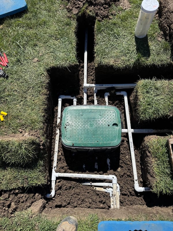 Green valve box with PVC lines branching out before backfill