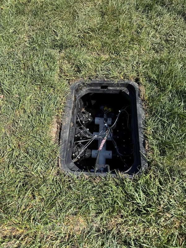 Open valve box in a lawn showing the sprinkler valves inside