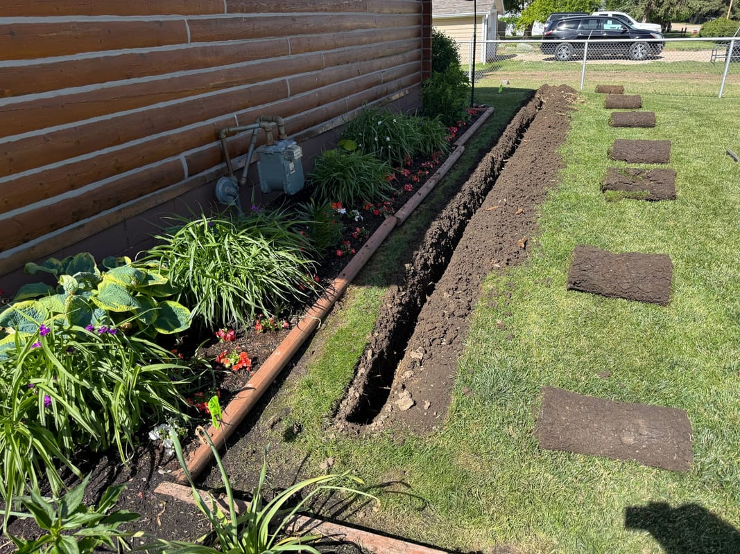 Narrow trench dug along a flower bed with sod squares set aside