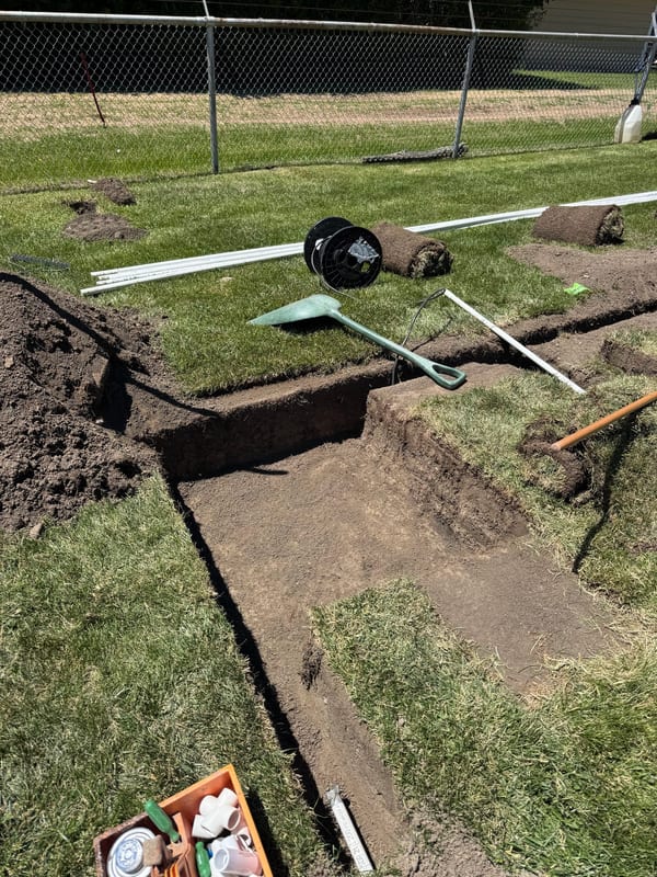 Open trenches in a lawn with pipe and tools laid out