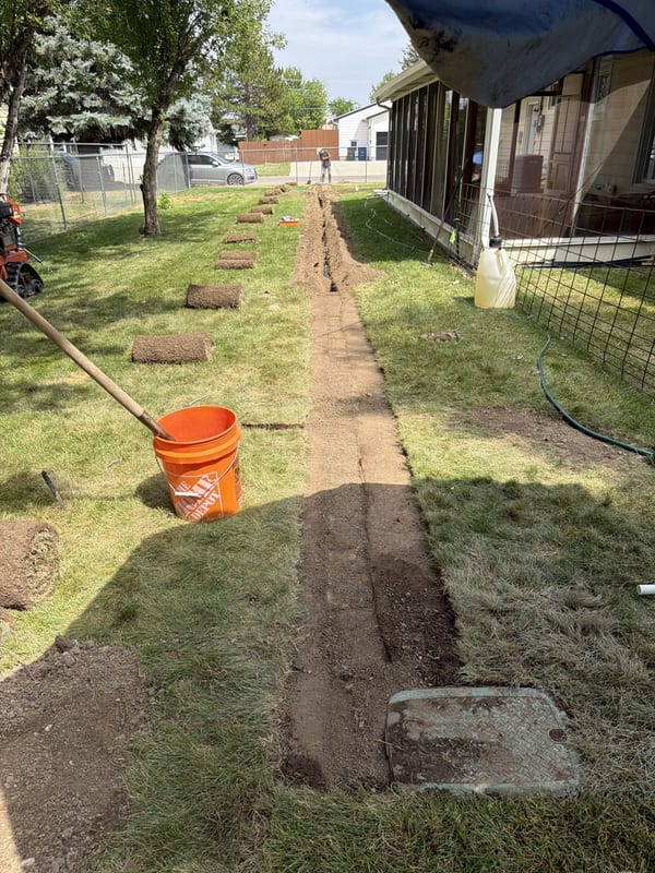 Trench dug across a back yard with sod squares cut and stacked