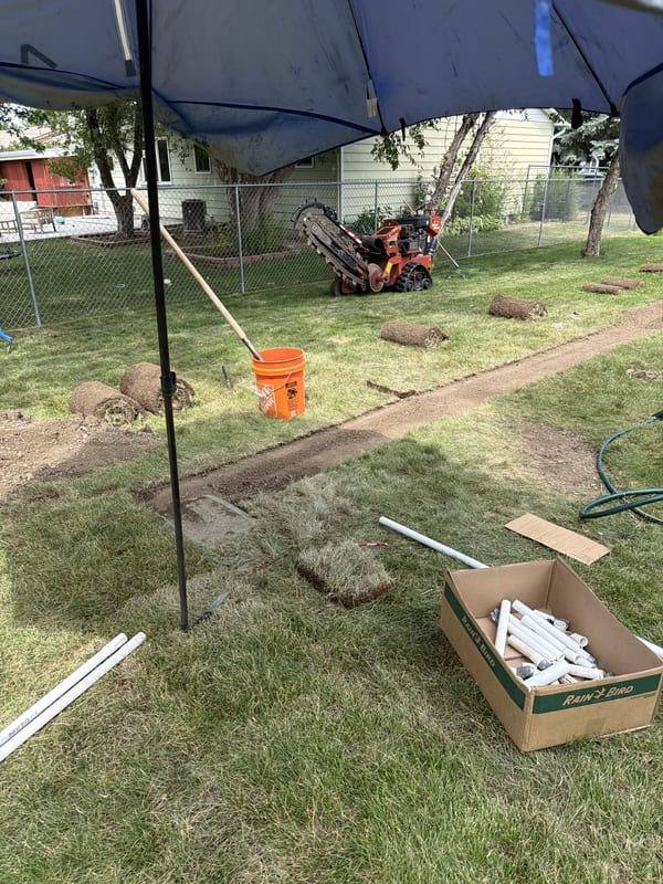 Trencher, pipe and supplies under a canopy during a backyard sprinkler install
