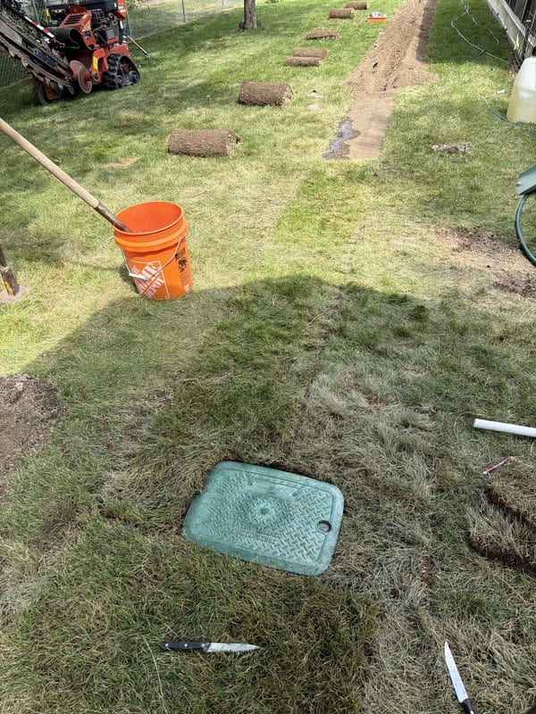 Green valve box lid set flush with the lawn beside a trench