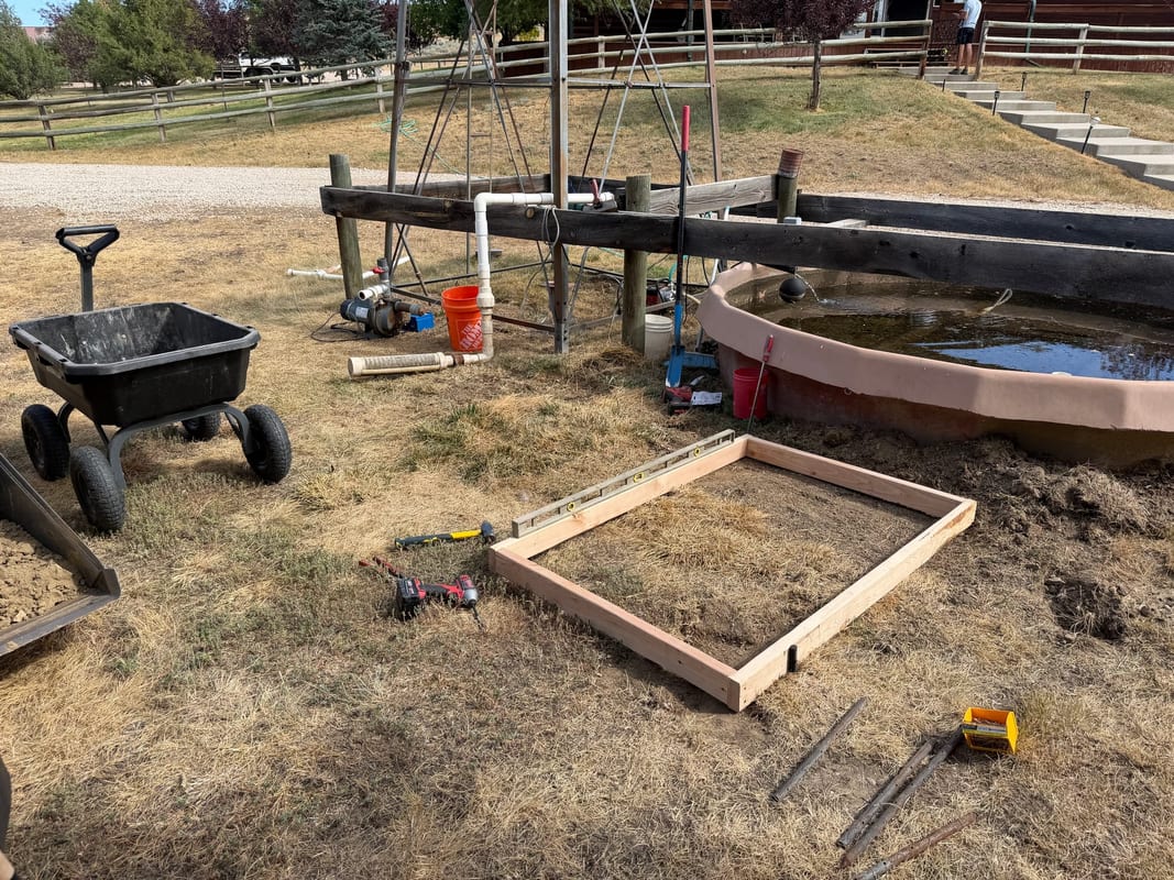 Wooden form for a concrete pump pad next to a stock tank on a rural property
