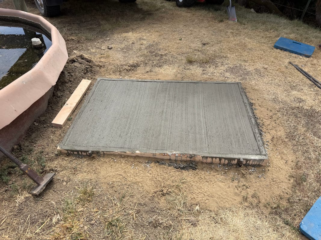 Freshly poured concrete pad next to a water tank