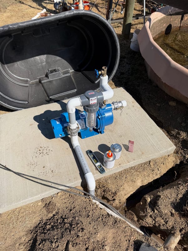 Blue irrigation pump plumbed on a concrete pad beside water tanks
