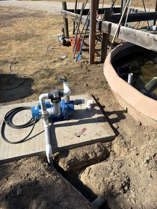 Irrigation pump on a concrete pad next to a stock tank with the supply line trenched